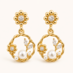 Pair of gold-tone floral pearl-style drop earrings on a warm white background